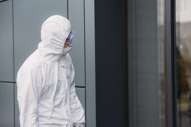 epidemiolog w kombinezonie ochronnym stojący na zewnątrz i patrzący przez okno budynku - Zdjęcie, obraz