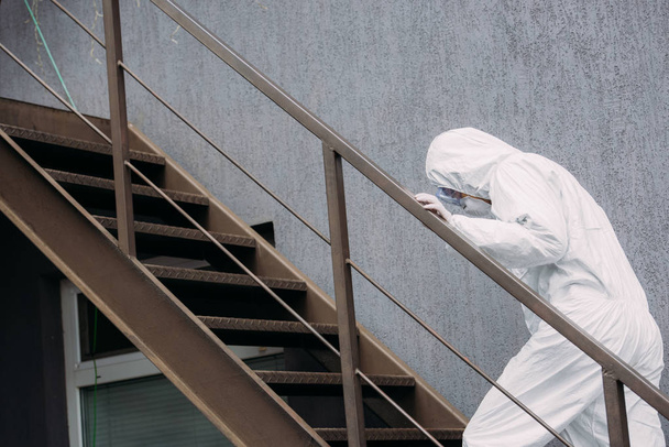 asian epidemiologist in hazmat suit and respirator mask walking upstairs outside building - 写真・画像
