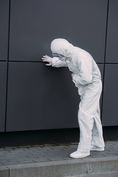 epidemiólogo asiático en traje de hazmat apoyado en la pared mientras que sufre de dolor abdominal sintomático
 - Foto, imagen