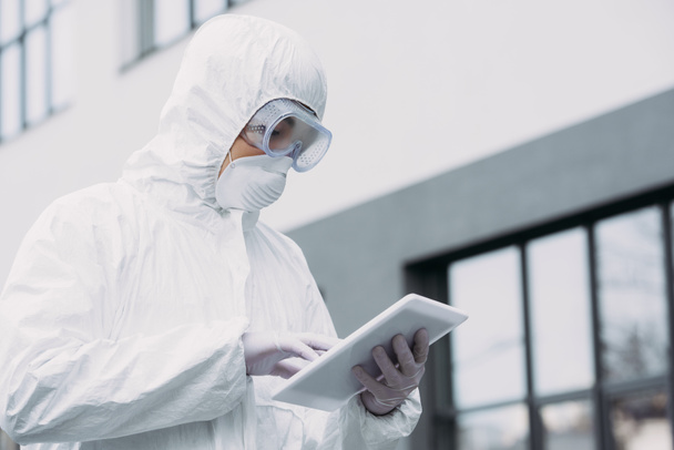 epidemiólogo asiático en traje de hazmat y máscara respiratoria usando tableta digital mientras está de pie en la calle
 - Foto, Imagen