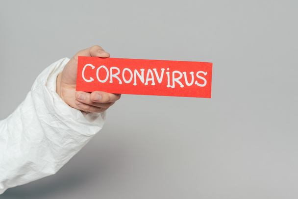 vista recortada del epidemiólogo con tarjeta de advertencia con inscripción de coronavirus sobre fondo gris
 - Foto, Imagen