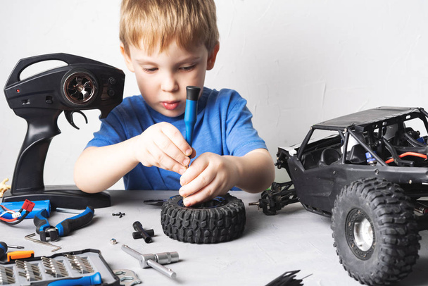 Radio controlled models: A little boy in a blue T-shirt is repairing his RC car buggy. - Фото, изображение