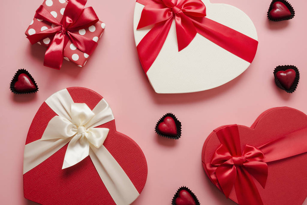 Valentines day greeting card. Pattern of red gift boxes heart shaped and chocolate sweets on pink. View from above. - 写真・画像