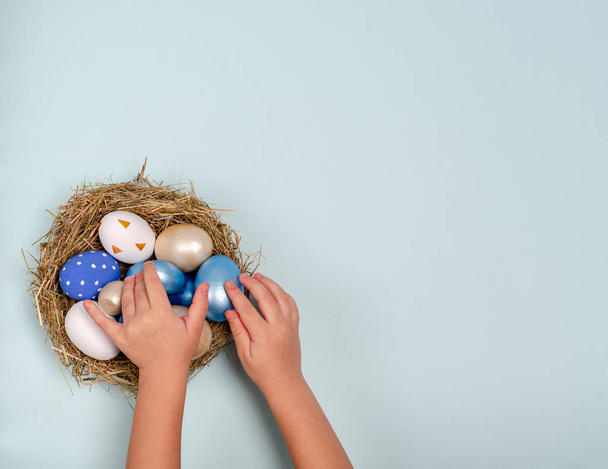 Childrens hands lay blue Easter eggs in a nest with eggs on a blue background with space for copy - Zdjęcie, obraz
