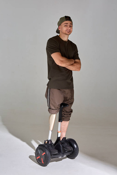 Disabled young man on hoverboard with leg prosthesis in the studio. Shadow light. - Foto, afbeelding