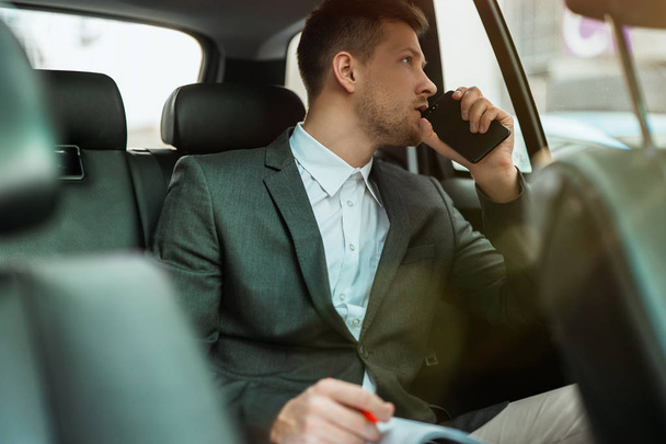 successful businessman with planner and smartphone sitting on back seat of car on way to meetting with partners, multitasking concept - Photo, image