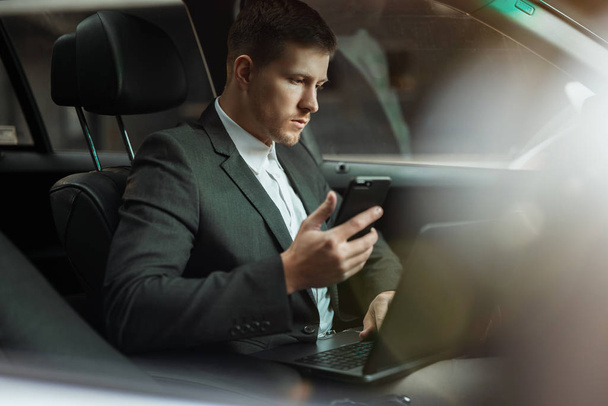 young businessman works in his car using his laptop and smartphone getting ready for important meetting , looks concentrated, multitasking concept - 写真・画像