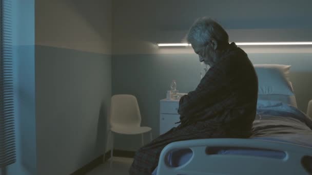 Samotny smutny senior siedzi na szpitalnym łóżku - Materiał filmowy, wideo