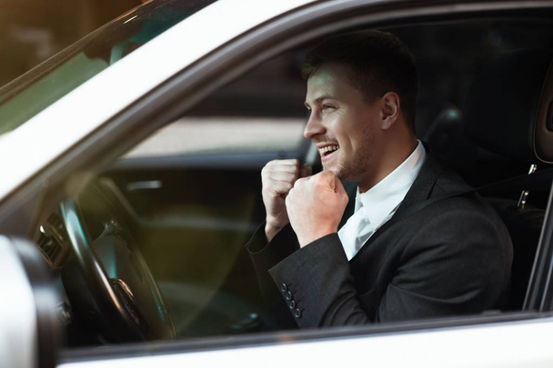 young smiling businessman sits in his car in winning position with his fists clenched, successful business strategy concept - Foto, imagen