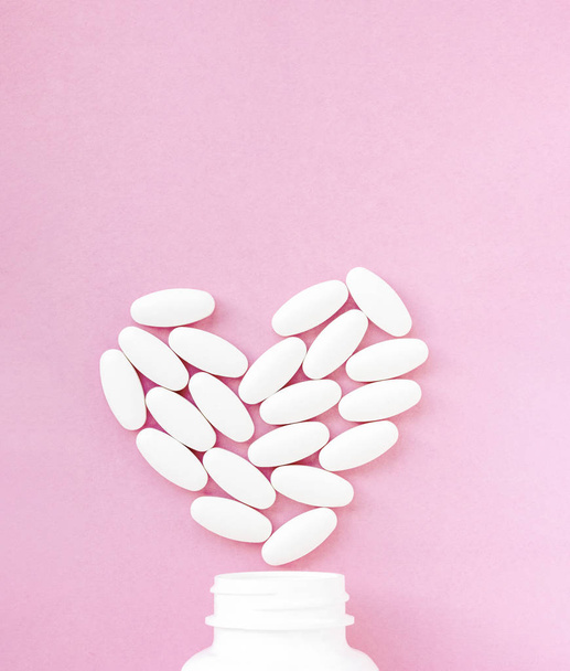 Weiße Pillen in Herzform mit Flasche auf rosa Hintergrund. Kopierraum für Text - Foto, Bild