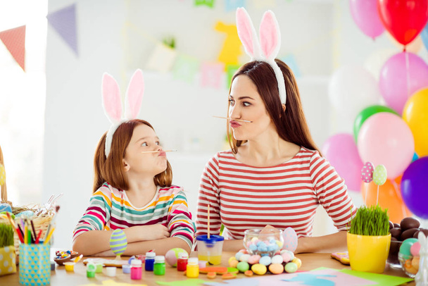 Close-up portrait of two nice attractive comic humorous playful cheerful girls small little pre-teen daughter wearing bunny ears holding pencil pout lips grimacing in white light interior room house - 写真・画像