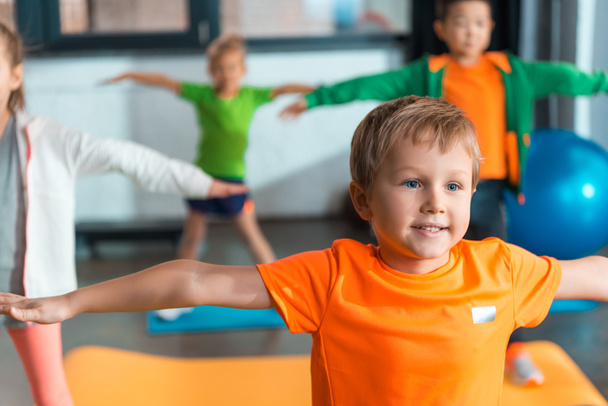 Selective focus of multiethnic kids doing exercise with outstretched hands in sports center - Fotoğraf, Görsel