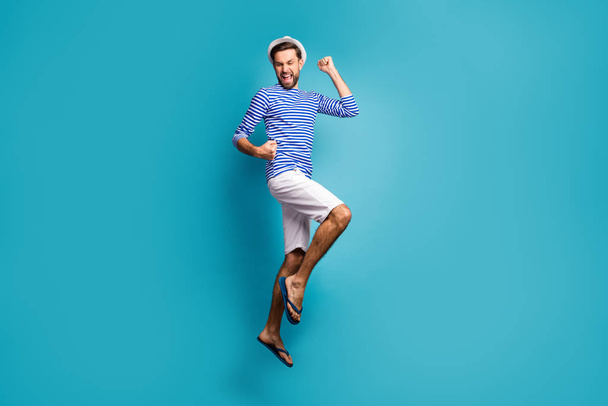 Full body profile photo of funky astonished guy tourist jump high celebrating vacation start wear striped sailor shirt vest cap shorts flip flops isolated blue color background - 写真・画像