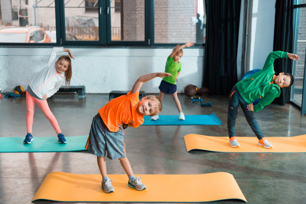 Niños multiculturales calentándose juntos en colchonetas de fitness en el gimnasio
 - Foto, imagen