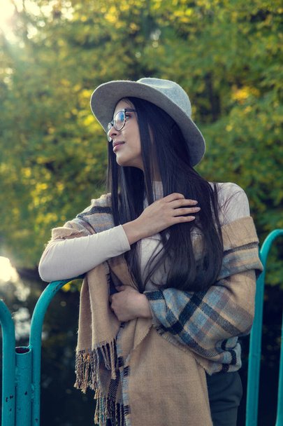 Close up of happy emotionally brunette woman with long hair and hat, smiling at camera. Beautiful model with perfect makeup after salon, posing in park. Concept of fashion and beauty. - Fotografie, Obrázek