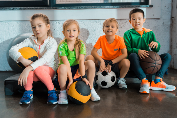 Enfants multiculturels assis sur des plates-formes pas à pas avec des balles dans la salle de gym
 - Photo, image