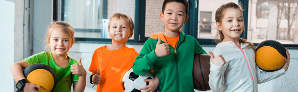 Widok z przodu szczęśliwy wielokulturowe dzieci trzyma piłki w siłowni, panoramiczny strzał - Zdjęcie, obraz