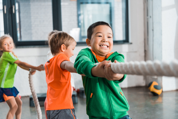 Selective focus of multicultural kids playing tug of war in gym - Fotó, kép
