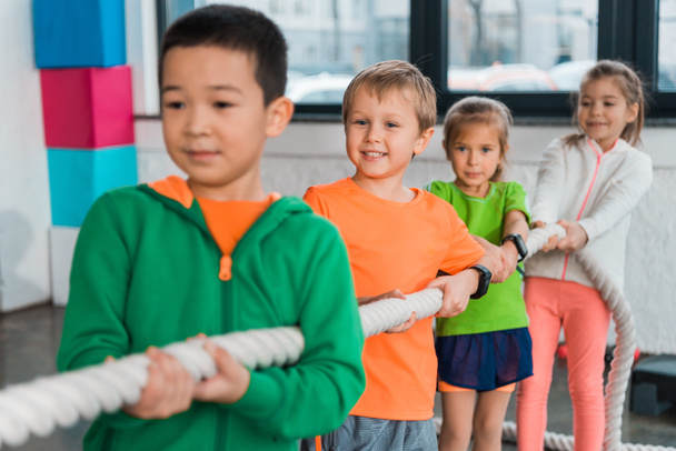 Selective focus of multiethnic children playing tug of war in sports center - Fotografie, Obrázek