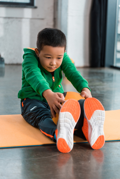 Asiatique garçon tenant ballon et étirement sur tapis de fitness dans la salle de gym
 - Photo, image