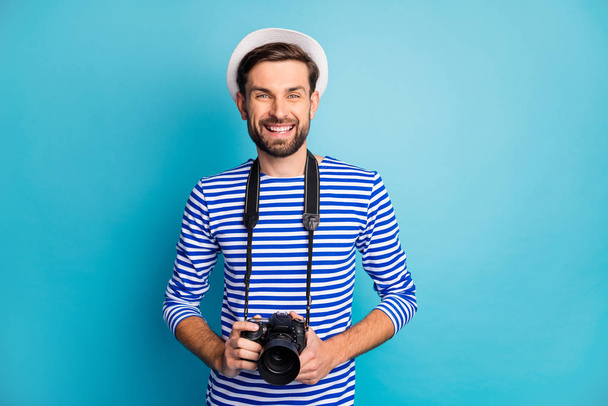 Photo of attractive guy photographer hold professional digital lens camera traveling abroad make pictures wear striped sailor shirt vest white cap isolated blue color background - Фото, зображення