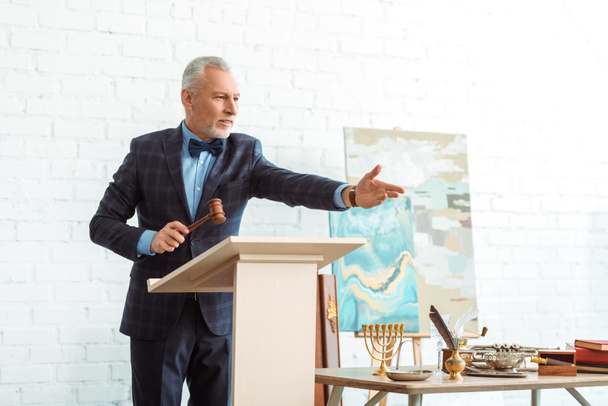 красивый аукционист держа деревянный молоток и указывая рукой во время аукциона
 - Фото, изображение