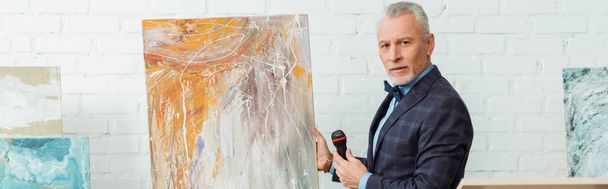 panoramic shot of auctioneer talking with microphone and standing near picture during auction - Fotoğraf, Görsel