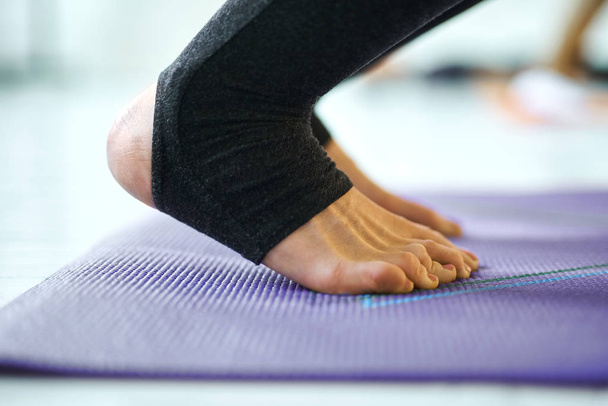 Close-up of woman legs on violet yoga or fitness mat indoor, doing yoga pose. - Foto, Imagem