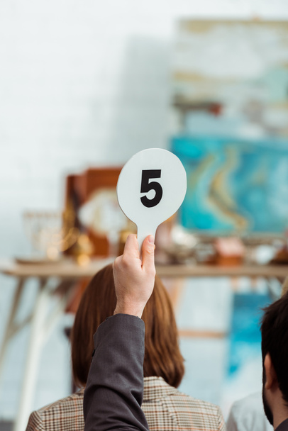 oříznutý pohled kupujícího ukazujícího aukční pádlo s číslem pět během aukce - Fotografie, Obrázek