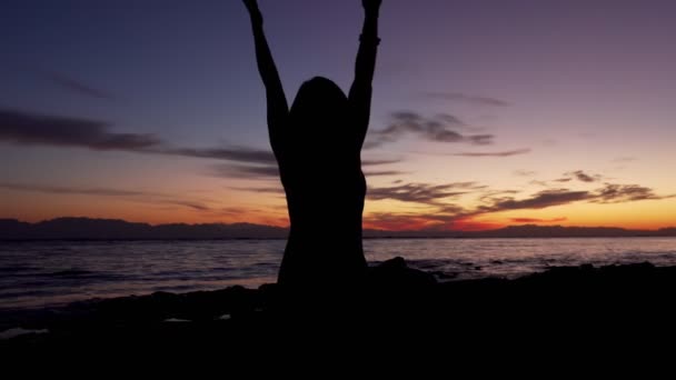 Silhueta de menina praticar meditação em pose de lótus pelo mar ao pôr do sol
 - Filmagem, Vídeo