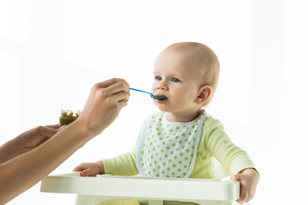 Matka ze słoikiem warzyw odżywiania niemowląt i łyżeczki karmienia niemowląt na krześle odizolowanym na białym - Zdjęcie, obraz