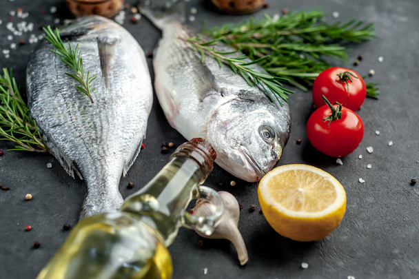 Fresh dorado fish with spices and ingredients tomato, rosemary, sunflower oil, lemon for cooking on a stone background - 写真・画像