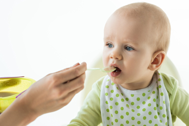 Selective focus of mother feeding adorable baby with puree isolated on white - Foto, Imagen