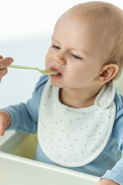 Hoge hoek uitzicht van moeder voeden zuigeling met babyvoeding op voederstoel op witte achtergrond - Foto, afbeelding