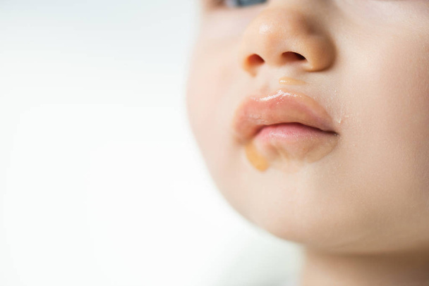 Vista de cerca del puré de frutas en la boca sucia del bebé aislado en gris
 - Foto, Imagen