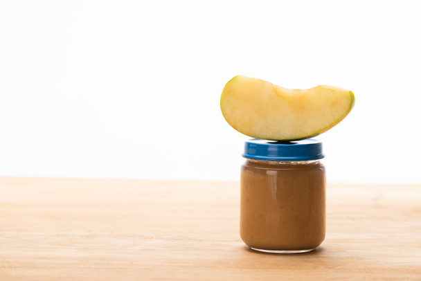 Kousek jablka na sklenici s ovocem výživa pro kojence na dřevěném povrchu izolovaném na bílém - Fotografie, Obrázek
