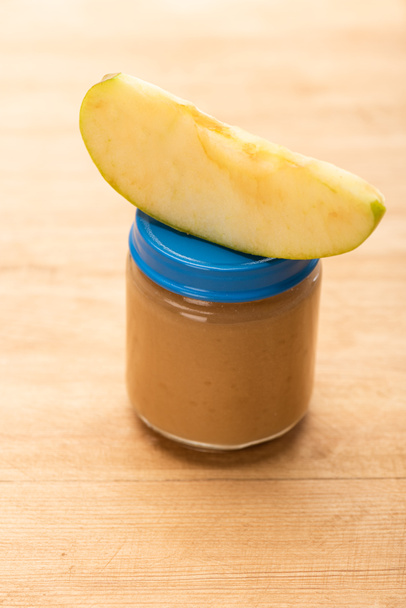 Close-up zicht op stukje appel op pot met fruit babyvoeding op houten ondergrond - Foto, afbeelding