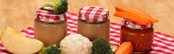 Colpo panoramico di vasetti di alimenti per l'infanzia con verdure fresche e mela su tovaglia su superficie di legno
 - Foto, immagini