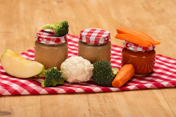Jars of vegetable baby nutrition with fresh vegetables and apple on napkin on wooden surface - Fotoğraf, Görsel