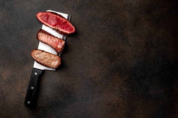 Trzy kawałki mięsa grillowane nad nożem do mięsa Trzy rodzaje smażonego mięsa, rzadkie, średnie, dobrze wysmażone przyprawami na kamiennym tle z kopią miejsca na tekst - Zdjęcie, obraz