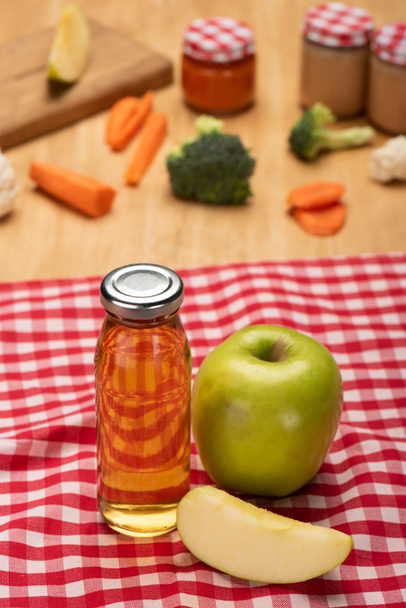 Selective focus of bottle with apple juice and jars of baby food with ingredients on tablecloth on wooden surface - Fotoğraf, Görsel