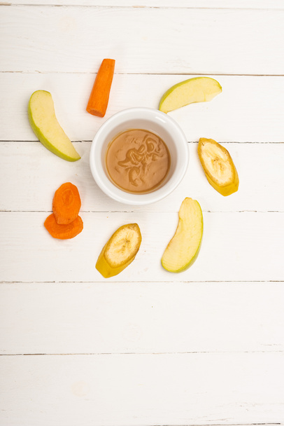 Vue du dessus des aliments pour bébés dans un bol avec des fruits tranchés et des carottes sur une surface en bois blanc
 - Photo, image