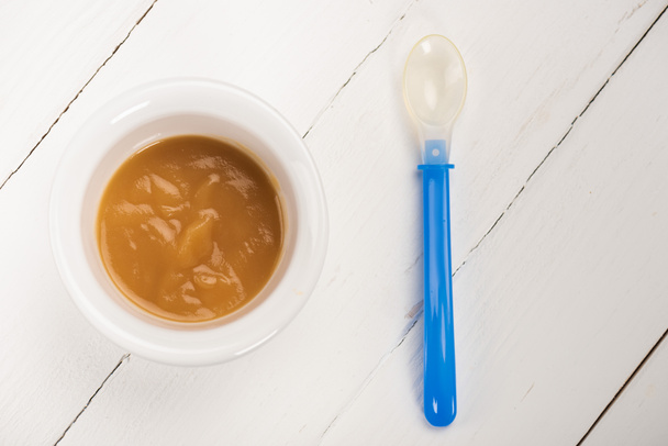 Top view of bowl with baby food and spoon on white wooden background - Foto, Imagem