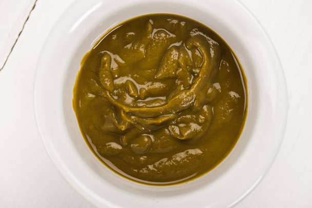 Вид сверху на детское питание из брокколи в миске на белой деревянной поверхности
 - Фото, изображение