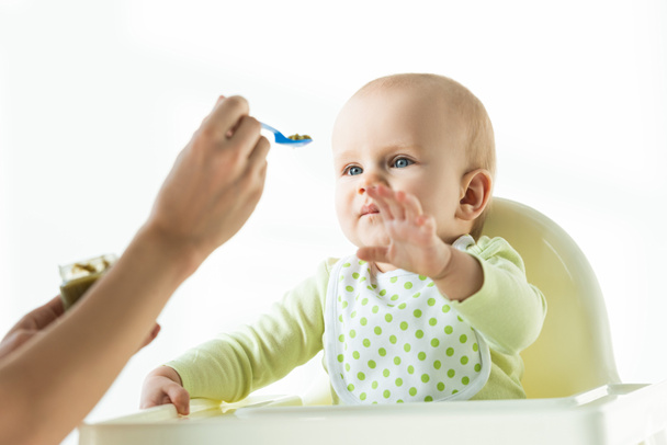 Concentration sélective de bébé mignon tirant la main à la mère avec cuillère de nutrition bébé isolé sur blanc
 - Photo, image
