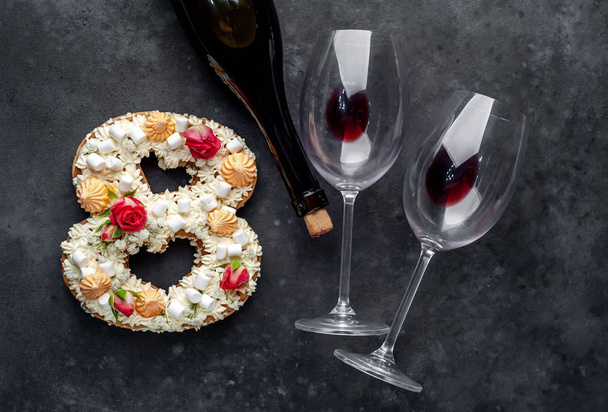 κέικ σε σχήμα 8 είναι διακοσμημένο με λουλούδια, τυρί κρέμα, marshmallows, Bizet με γυαλιά σε ένα πέτρινο φόντο, γιορτή έννοια δείπνο για δύο στις 8 Μαρτίου. - Φωτογραφία, εικόνα