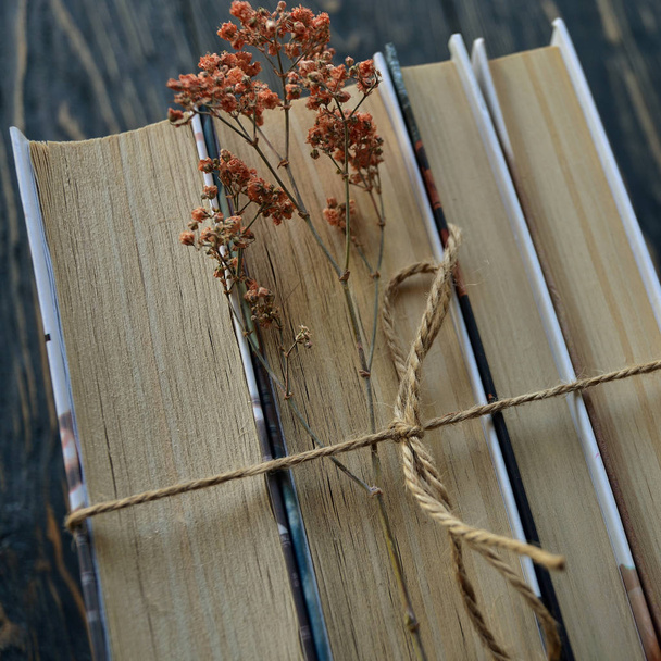 ein Stapel Bücher mit Bindfäden und getrockneten Blumen auf dunklem Holzgrund. Ansicht von oben. Nahaufnahme. flache Lage. - Foto, Bild