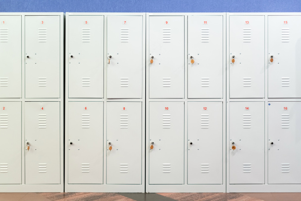 A row of grey metal school lockers with keys in the doors. Storage locker room in corridor of educational institution - Photo, Image