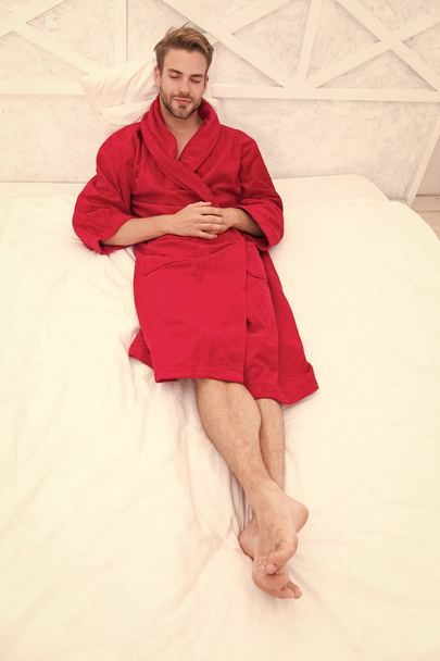 Knowing how to relax. Handsome man lying in bed to relax after bath. Sleepy guy in red bathrobe taking time to relax in morning. Its time to relax - Foto, Imagem