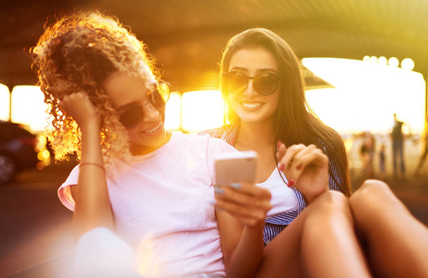 Zwei junge Mädchen amüsieren sich an einem Sommertag mit Sonnenlicht auf Einkaufswagen. Junge Freunde haben Spaß und machen gemeinsam ein Selfie am Telefon. Lifestyle, Freizeit, Unterhaltung, Jugendkonzept.                 - Foto, Bild